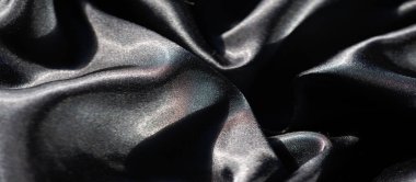 Parlak parıltılı siyah kumaş bulanıklığı. Zarif bir şekilde yumuşak dalgalara dönüşmüş. Doku ve ışıltı, yüzey boyunca ışık ve gölgenin etkileşimini vurgular ve bileşime derinlik katar..