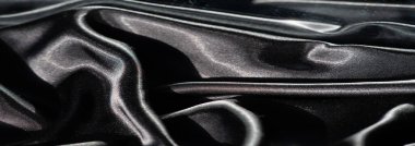 Siyah saten kumaş bulanıklığı zarif bir şekilde bükülmüş ve karmaşık kıvrımlar oluşturuyor. Işıldayan yüzey ışık ve gölgeyle oynar, derinlik ve hareket hissi yaratır..