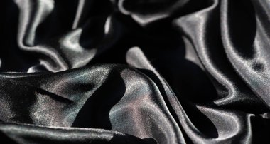 Soyut kıvrımlarda siyah saten kumaş bulanıklığı, keskin röfleler ve derin gölgeler, düz yüzeyi boyunca ışık ve karanlık arasında yüksek kontrastlı bir etkileşim yaratıyor..