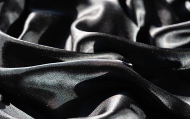 Soyut kıvrımlarda siyah saten kumaş bulanıklığı, keskin röfleler ve derin gölgeler, düz yüzeyi boyunca ışık ve karanlık arasında yüksek kontrastlı bir etkileşim yaratıyor..