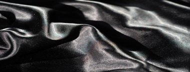 Soyut kıvrımlarda siyah saten kumaş bulanıklığı, keskin röfleler ve derin gölgeler, düz yüzeyi boyunca ışık ve karanlık arasında yüksek kontrastlı bir etkileşim yaratıyor..