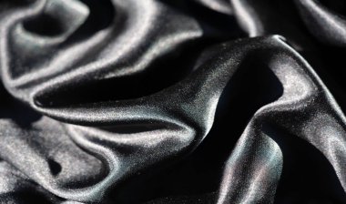 Bükülmüş siyah kumaş bulanıklığı karmaşık dalgalar ve kıvrımlar oluşturuyor. Parlak yüzey ışığı yakalar ve bu zarif soyut kompozisyonda parlak ve derin gölgeler arasında bir oyun yaratır..