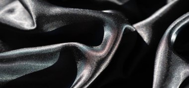 Pürüzsüz yüzeyinde dans eden ışık ve gölgelerle zarif dalgalar halinde katlanmış siyah saten kumaştan bir bulanıklık. Yüksek parlaklık parıltısı bu zarif parçaya derinlik ve doku ekler..
