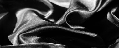 Siyah kumaş bulanıklığı dinamik şekillerde kıvrılmış ve yüzeyleri parıldıyor. Işık pürüzsüz kumaştan yansıyarak gölgelerin ve gölgelerin çarpıcı zıtlıklarını yaratır..