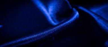 Görüntü, parlak mavi kumaşın derin kıvrımlı ve zıt ışıkla yakın plan görüntülerini verdi. Gölgelerin ve yansımaların dinamik etkileşimi akıcılık ve zenginlik hissi yaratır..