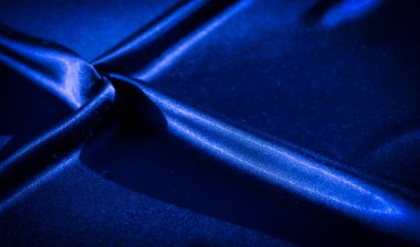 Görüntü, parlak mavi kumaşın derin kıvrımlı ve zıt ışıkla yakın plan görüntülerini verdi. Gölgelerin ve yansımaların dinamik etkileşimi akıcılık ve zenginlik hissi yaratır..