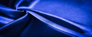 Karmaşık kıvrımları ve parlak gölgeleri olan ipek mavisi bir kumaşın bulanık yakın plan görüntüsü. Parlak doku ve yumuşak akış çizgileri lüks ve canlı bir his yaratır..