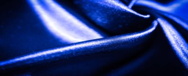 Pürüzsüz mavi saten kumaşın bulanık ve soyut yakın çekimi yumuşak kıvrımlara dönüşmüş koyu mavi tonlar ve parlak yüzey kumaşa dinamik bir akış sağlıyor lüks ve hareketli insanlar hissi yaratıyor.