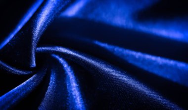 Zarif kıvrımları ve ince kıvrımları olan koyu mavi kumaşın bulanık görüntüsü. Pürüzsüz, parlak yüzey ışığı yansıtıyor, lüks ve akışkan bir doku yaratıyor, soyut tekstil tasarımları için mükemmel..