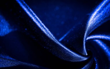 Zarif kıvrımlara ve dalgalı dalgalara sahip koyu mavi kumaş bulanıklığı, pürüzsüz yüzeyinde ışığı yansıtıyor. Malzemenin yumuşak parıltısı ve bükülme şekli akışkan hareket ve lüks hissi verir..