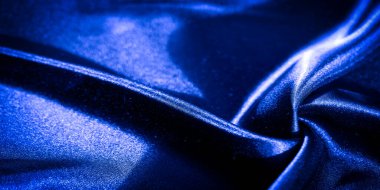 Derin mavi kumaştan oluşan bulanık kıvrımlar, parlak, saten dokusunu vurgulamak için ışık yüzeyde hafifçe oynuyor. Örtülü malzeme dinamik ve zarif bir görsel efekt yaratır.