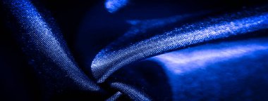 Yumuşak kıvrımlı ve parlak yüzeyi olan koyu mavi kumaştan bir bulanıklık. Yumuşak doku ve ışık yansıması maddeye derinlik ve zenginlik hissi verir..