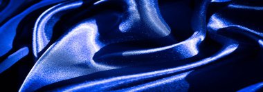 Dinamik kıvrımları ve zengin bir dokusu olan canlı mavi kumaş bulanıklığı. Işık parlak yüzeyi güçlendiriyor, parlak ve lüks bir görsel cazibe yaratıyor..