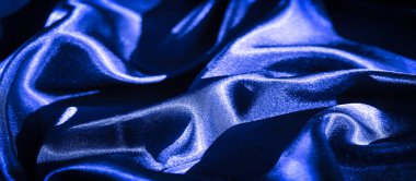 Bulanık mavi saten kumaş yumuşak dalgalanan dalgalarla pürüzsüzce akıyor. Parlak madde ışığı yansıtır, zengin, lüks mavi tonunu yükseltir ve dinamik bir yüzey yaratır..