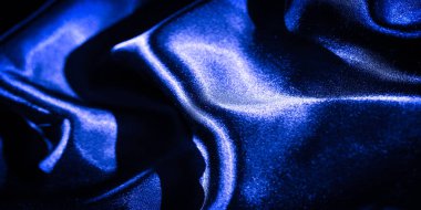 Karmaşık kıvrımlı bulanık mavi saten kumaş lüks ve parlak bir yüzey oluşturuyor. İpeksi doku ve yansıtıcı bitiş kumaşın zengin mavi tonlarına derinlik ekler..