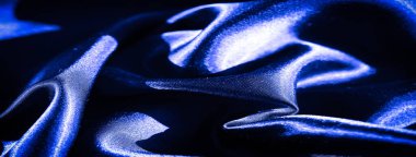 Karmaşık kıvrımları ve parıldayan bir dokusu olan zengin, asil mavi saten kumaş bulanıklığı, ışık yansımalarını ve lüks, soyut bir şekilde pürüzsüz dalgaları yakalıyor..