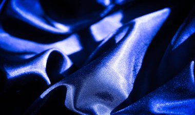 Yumuşak dalgalar ve kıvrımlar halinde akan koyu mavi saten kumaş bulanıklığı zarif bir kompozisyon için yayılmış ışıkla aydınlatılan ince ve parlak bir doku yaratıyor..