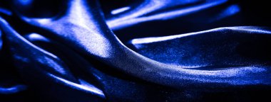 Yumuşak dalgalar ve kıvrımlar halinde akan koyu mavi saten kumaş bulanıklığı zarif bir kompozisyon için yayılmış ışıkla aydınlatılan ince ve parlak bir doku yaratıyor..