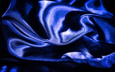 Parlak kıvrımlarla süslenmiş mavi saten kumaş bulanıklığı. Kumaş ışığı yumuşak, dalgalı kıvrımlarda yansıtır, satene lüks ve pürüzsüz bir doku verir, koyu mavi renkler zarafet katar..