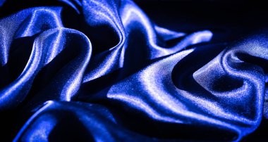 Koyu mavi saten kumaşlı, zarif kıvrımlı ve zengin desenli. Parlak, pürüzsüz yüzey ışığı yansıtıyor, kompozisyona biraz lüks ve tarz katıyor..