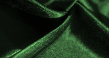 Görüntü. Yansıtıcı ışıkla vurgulanmış zarif yeşil saten kumaş kıvrımları lüks ve pürüzsüz bir doku yaratır. Yumuşak kumaş bir sofistike hissi uyandırıyor..