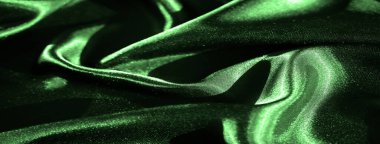 Zengin yeşil saten kumaşın bulanık kıvrımları yumuşak dokuyu ve maddenin yansıtıcı doğasını vurguluyor. Işık ve gölge, parlak yüzeyde güzel bir etkileşim içinde..