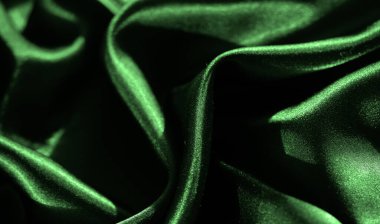 Yeşil saten kumaşın bulanık kıvrımları, parlak ve yansıtıcı dokusunu sergiliyor. Işık ve gölgeler zarif kıvrımları güçlendirir, lüks ve sofistike bir görünüm verir..