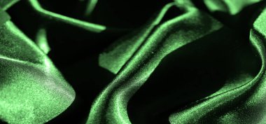 Bulanık yeşil saten kumaş sıvı yaratır. İnce gölgeler ve parlak ışık yansımalarıyla gelişen dalgalı dokular. Katlar lüks ve sofistike bir şekilde yayılan zarif, yumuşak bir desen oluşturuyor.