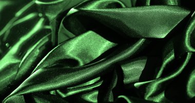 Bulanık yeşil saten kumaş, pürüzsüz ve akışkan kıvrımları yakına çekiyor. Parlak yüzey ışığı güzel yansıtıyor, tekstilin zarafetini ve lüksünü vurguluyor..