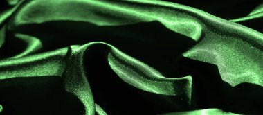Canlı yeşil saten kumaş bulanıklığı, kumaşın pürüzsüz kıvrımlarını ve yumuşak dokusunu yakın çekimde yakalıyor. Derin gölgeler, kumaşın yüzeyindeki ipeksi, lüks hissi güçlendirir..