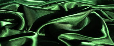 Yumuşak dalgalarda yakalanan canlı yeşil saten kumaş bulanıklığı, pürüzsüz, ipek dokusunu ve lüks parıltısını gözler önüne sermek için ince gölgelerle aydınlatılmış..