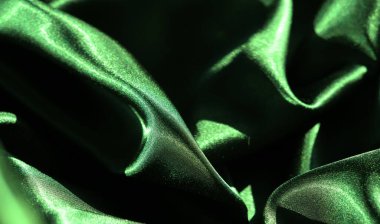 Yumuşak ve dalgalı kıvrımlı yeşil saten kumaşın bulanık görüntüsü. Parlak yüzey ışığı güzel yansıtıyor, kumaşın lüks ve ipeksi dokusunu vurguluyor..