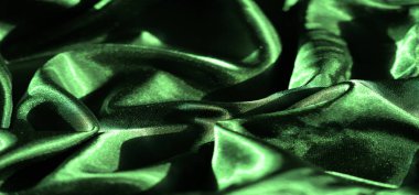 Yumuşak ve dalgalı kıvrımlı yeşil saten kumaşın bulanık görüntüsü. Parlak yüzey ışığı güzel yansıtıyor, kumaşın lüks ve ipeksi dokusunu vurguluyor..
