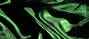 Pürüzsüz, akışkan kıvrımlı ve parlak parıltılı yeşil saten kumaştan bulanık bir görüntü. Işık yüzeyden yansıyarak, kumaşın lüks ve yumuşak dokusunu vurgular..
