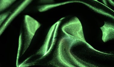 Yumuşak ve dalgalı kıvrımlı yeşil saten kumaşın bulanık görüntüsü. Parlak yüzey ışığı güzel yansıtıyor, kumaşın lüks ve ipeksi dokusunu vurguluyor..