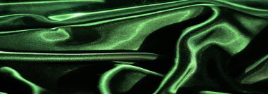 Yumuşak ve dalgalı kıvrımlı yeşil saten kumaşın bulanık görüntüsü. Parlak yüzey ışığı güzel yansıtıyor, kumaşın lüks ve ipeksi dokusunu vurguluyor..