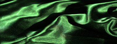 Yüksek yeşil saten kumaşlı, belirgin kıvrımlı, gölgeli ve ipeksi dokuya derinlik katan bir bulanıklık. Yakın plan, dramatik ışıklandırmada kumaşın lüks parıltısını yakalar..