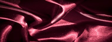 Görüntü, parlak bir parıltıyı düşük ışıkta yansıtan karmaşık kıvrımlı kırmızı saten kumaşı yakalıyor. Kumaşın pürüzsüz akışı soyut bir görsel ritim yaratır..