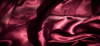 Yumuşak, zarif kıvrımlı parlak bir kaplama ile örtülmüş lüks kırmızı saten kumaş bulanıklığı. Malzemenin zengin dokusu ışığı yakalar ve kumaşa derinlik ve parlak bir görünüm ekler..
