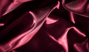 Kırmızı saten kumaş bulanıklığı zarif kıvrımların çaprazında. Parlak dokusu ve koyu kırmızı rengi kumaşa lüks ve zarif bir görünüm verir..