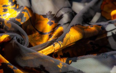 Saf bir malzeme üzerinde altın sarısı taç yaprakları ve siyah yapraklar. Moda veya dekor için mükemmel ama zarif bir çiçek kompozisyonu sunuyor..