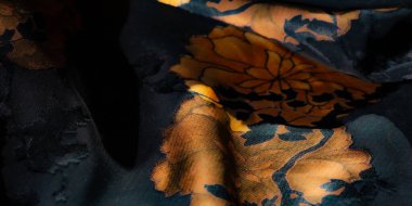 Görüntü. Bu katıksız kumaş üzerindeki siyah ve turuncu çiçekli motiflerin zarif karışımı zengin, katmanlı bir doku yaratıyor. Gölgeler ve gölgeler, kumaşın yumuşak kıvrımlarına derinlik katıyor..