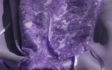 Parlak boncuklarla süslenmiş narin mor dantel kumaş bulanıklığı. Işıkla hafifçe aydınlatılmış. Karmaşık dokusu ve nazik kıvrımları kompozisyona lüks ve zarif bir his katıyor..