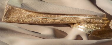 Karmaşık çiçek desenli bulanık altın dantel bej bir arkaplan üzerinde akar, parlak altın detaylar ve zarif kurdele bağları ile vurgulanan yumuşak kumaş.