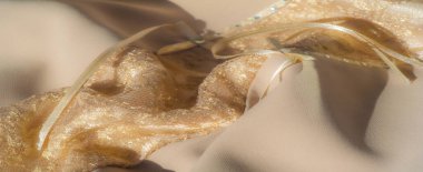 Altın dantel aksanlı ve kurdeleli, küçük mavi boncuklarla süslenmiş zarif bej kumaş bulanıklığı. Yumuşak dokusu ve nazik kıvrımları zarif ve narin bir görünüm yaratıyor..