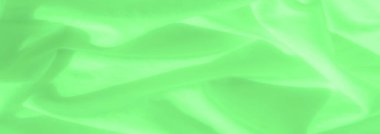 Yeşil saten kumaştan bulanık, pürüzsüz kıvrımlar ve yumuşak ışık malzemeden yansıyarak rüya gibi ve akışkan bir doku oluşturuyor. Parlak yeşil renk çarpıcı bir görsel cazibe katıyor.