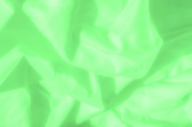 Kumaşın üzerinde yumuşak ve sıvı dalgalanmalar içeren yeşil saten kumaş bulanıklığı. Narin yeşil ton ve pürüzsüz yüzey, arka planlar için mükemmel, sakin ve rafine bir tekstil tasarımı yaratır..