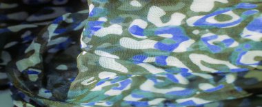 Görüntü. Mavi, yeşil ve beyaz soyut kamuflaj desenli yumuşak, hafif kumaş. Doku hassastır, karmaşık kıvrımları ve yumuşak ışıklandırmasıyla..