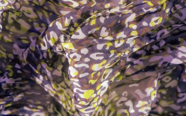 Soyut desenli, parlak mor, kahverengi ve yeşil tonlarda bulanık bir kumaş. Madde katmanlı ve dokulu görünüyor, kompozisyon boyunca derinlik ve hareket hissi yaratıyor..