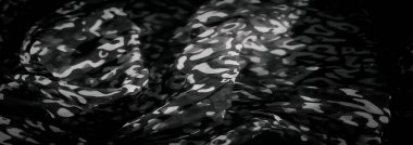 Gri tonlu, soyut kamuflaj benzeri desenlere sahip bulanık bir kumaş. Çarpıcı bir karşıtlık yaratan, akıcılık ve hareket hissi uyandıran açık ve koyu tonların karışımı..